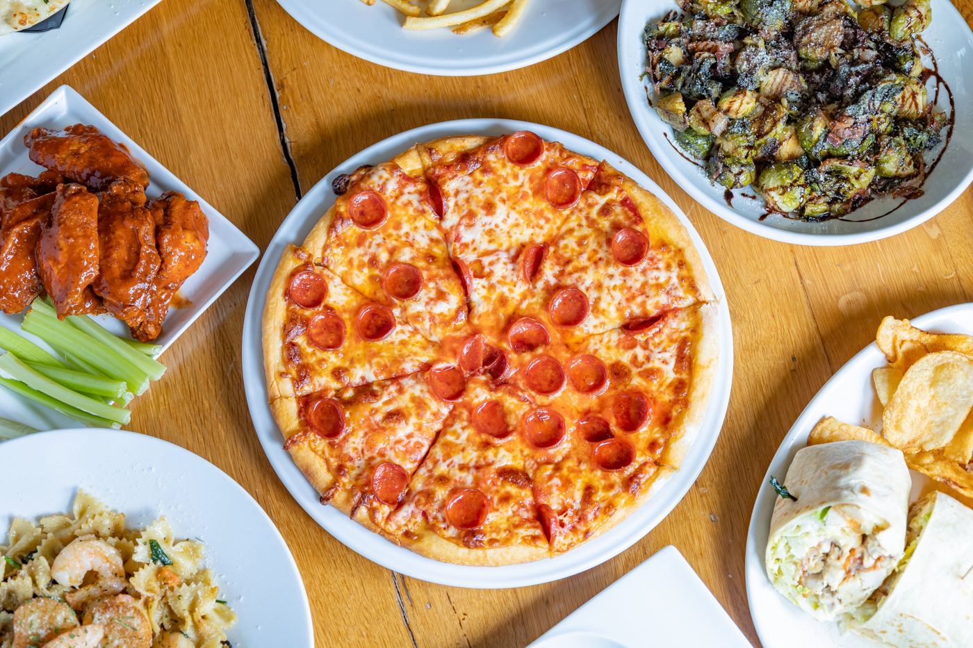 Pizza, wings, pasta and Brussels sprouts on a farm table
