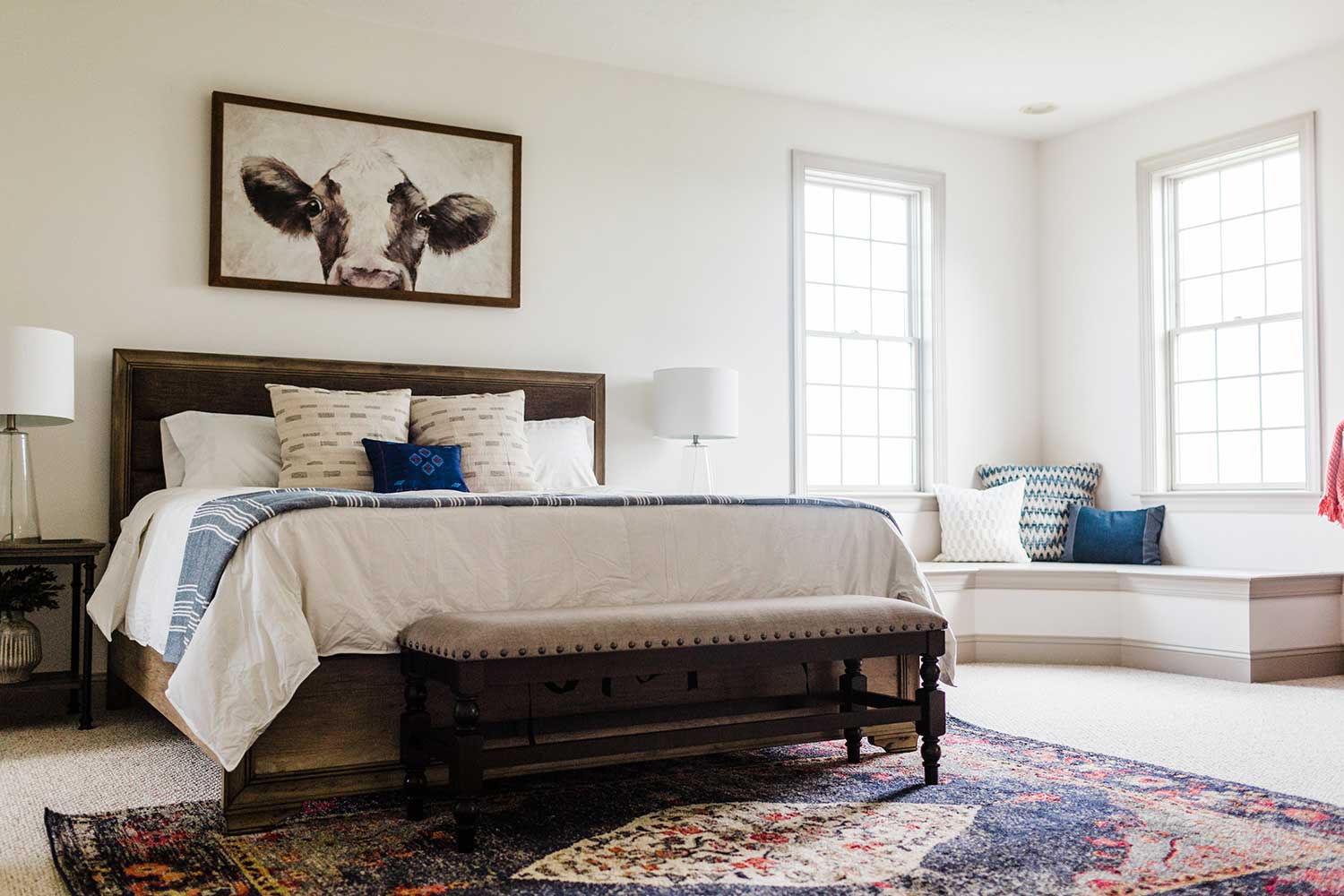 A bedroom with a window seat and a cow print above the bed