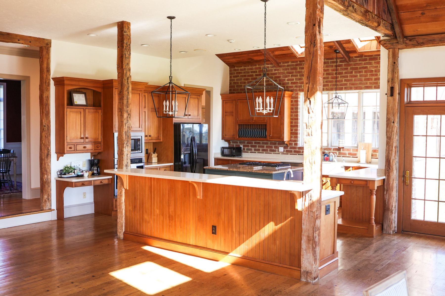 The kitchen with a long island, timber beams and a brick wall