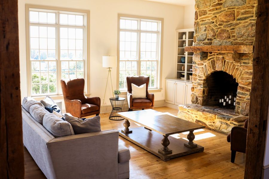 The living room with leather chairs, tall windows and a stone fireplace